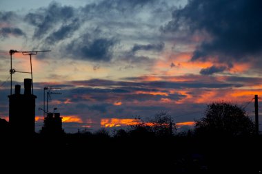 Karanlık çöktüğünde, çatıları siluetle kaplı kırmızı bir gökyüzü.