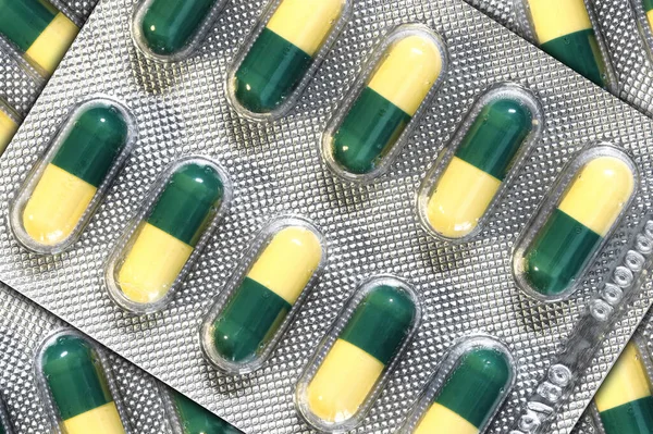 Green and yellow capsules for medication purposes in blister packs closeup