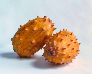 Bir çift dikenli kiwano meyvesi, beyaz bir arka planda, güneş ışığıyla aydınlatılmış.