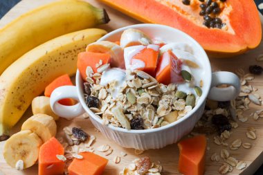 Sağlıklı kahvaltı, müsli, yoğurt, taze muz ve papaya karışımı beyaz kasede.