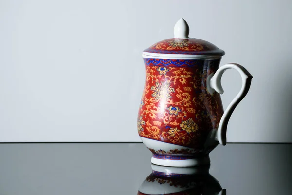 一个红色茶壶 上面有图案 放在一个白色背景的反光桌子上 — 图库照片