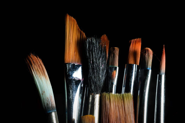 Paint brushes of different size are kept side by side in a dark background