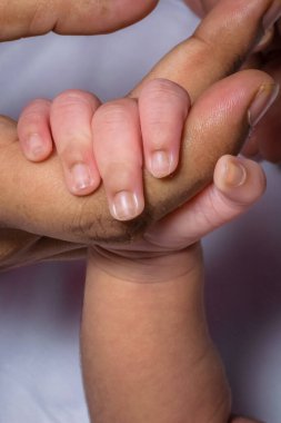 Yeni doğmuş bir bebek annesinin işaret parmağını sıkıca tutuyor. Beyaz arkaplan portresi