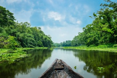 Etrafı yeşilliklerle çevrili bir köyden geçen saydam suyu olan bir nehir manzarası. Yukarıdaki mavi gökyüzü sudaki yansımasıyla