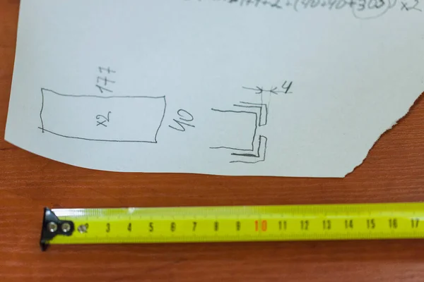 drawing with calculations and yellow metric measuring tape on the table, close up, blurry background