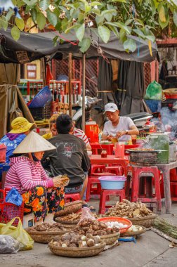 Hoi An Old Town / Vietnam - Mart 06: 2019: Sokak pazarında sebze satan bir kadın satıcı. İnsanlar sokak yemeği yiyor..