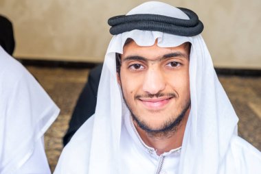 Müslüman adam Arap kıyafetleri içinde ailesiyle oturup Kuran okuyor.