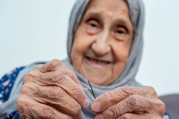 Arabic muslim old woman inserting thread in needle