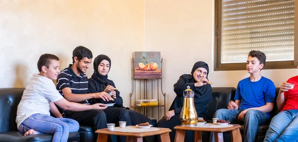 Happy arabic family sitting together enjoying arabic coffee and sweets and talking to each other