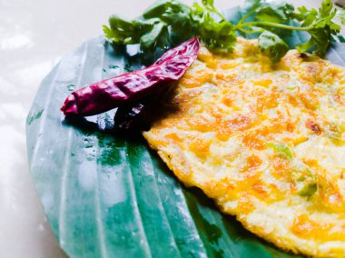 Kişniş yapraklı omlet ve muz yaprağında kırmızı biber. Muz yaprağı yeşil, biberler kırmızı ve omlet iyi kızartılmış. Muz yaprağında çizgiler var.