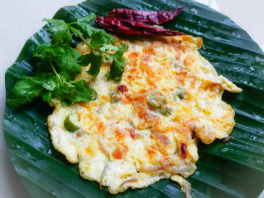 Kişniş yapraklı yumurta omleti ve muz yaprağında kırmızı biber. Muz yaprağı yeşil, biberler kırmızı ve omlet iyi kızartılmış. Muz yaprağının üzerinde çizgiler var..