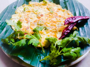 Kişniş yapraklı omlet ve muz yaprağında kırmızı biber. Muz yaprağı yeşil, biberler kırmızı ve omlet iyi kızartılmış. Muz yaprağında çizgiler var.