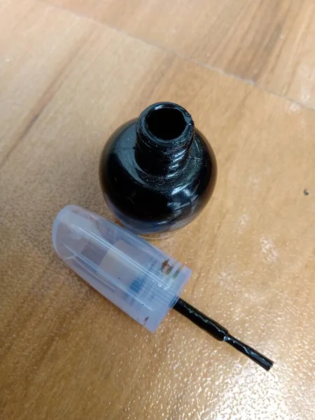 An opened Nail polish bottle and its brush placed on the table.Can see the black color nail polish bottle on it.