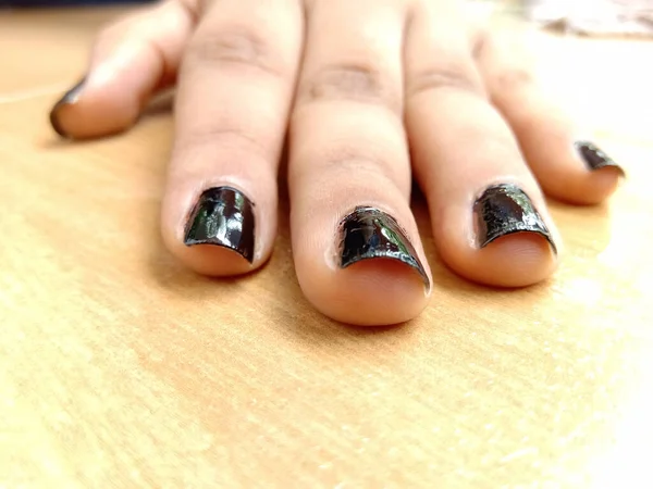 A closeup shot of a black nail polished hand placed on a table top from the front side.Hand have a beautiful skin tone color and softness.Glossy Black have a reflecting surface on the nails.