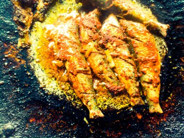 Kızartma tavasında iki sardalya kızartmak. Tavanın arka planında koyu renk ve balık iyice temizlenmiş. Tavada kızartılacak beş balık var ve Masala sarı ve kırmızı renk veriyor..
