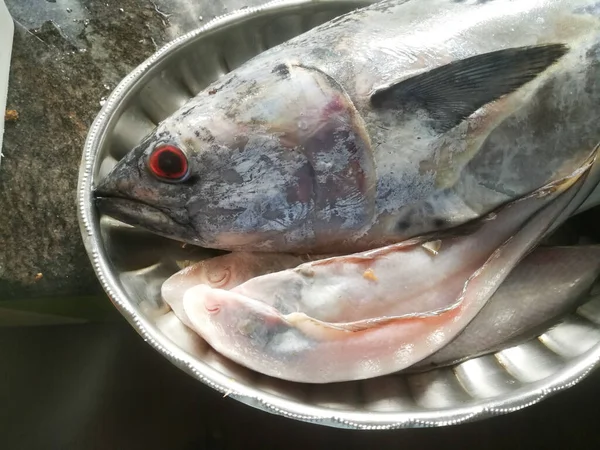 Raw Sea fish with red eyes in a steel plate which is special to make kerala style fish curry.The fish has red eyes and black at its center.The fins are also visible.