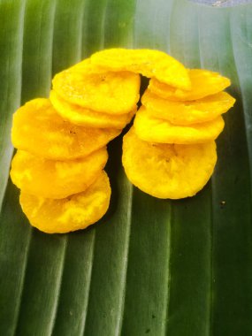 Muz yaprağına konmuş özel kızarmış muz cipsleri. Cipsler birbirinin üstüne istiflenmiş. Cipsler sarımsı renkte..