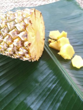 Ananas ve dilimleri yeşil bir muz yaprağına yerleştirilir. Dolu bir ananasın çapraz kesimi görülebilir. Parçaları yanına yerleştirilir..