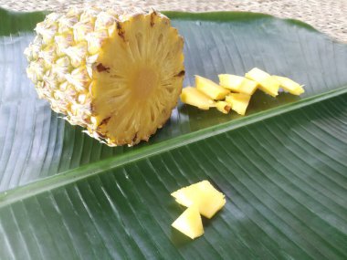 Ananas ve dilimleri yeşil bir muz yaprağına yerleştirilir. Dolu bir ananasın çapraz kesimi görülebilir. Parçaları yanına yerleştirilir..