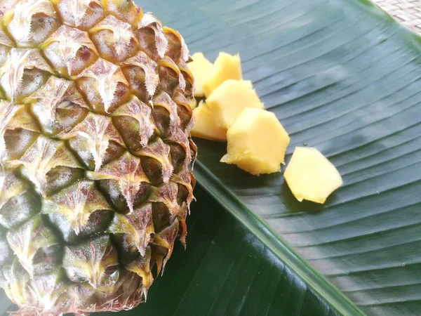 Ananas ve dilimleri yeşil bir muz yaprağına yerleştirilir. Dolu bir ananasın çapraz kesimi görülebilir. Parçaları yanına yerleştirilir..
