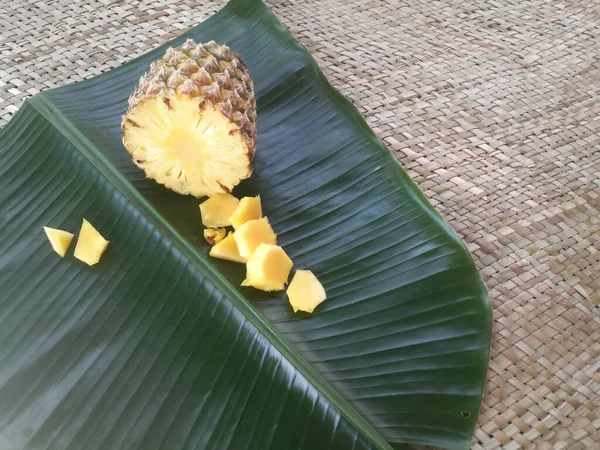 Ananas ve dilimleri yeşil bir muz yaprağına yerleştirilir. Dolu bir ananasın çapraz kesimi görülebilir. Parçaları yanına yerleştirilir..