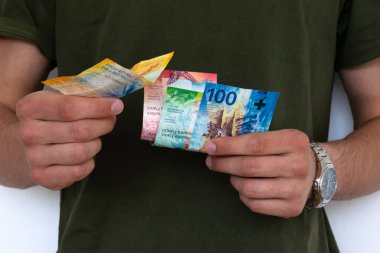 Genç adam banknot veriyor, İsviçre frangı. 10, 20, 50, 100 banknot büyüklüğünde. Bileğinde saat olan bir adam..