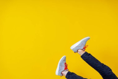 Alttan sarkan ayaklar, sarı arka planda spor ayakkabıları, kırmızı bağcıklar, moda blogu veya dergisi konsepti, minimalist ayakkabı arka planı, spor