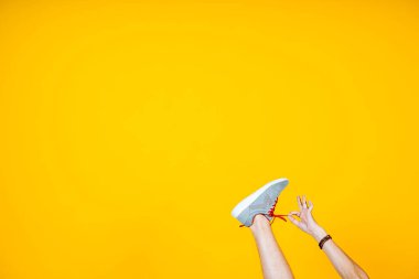 Sarı arka planda bir spor ayakkabısı içinde ayak, bağcıkları çözer