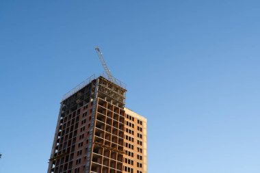 Mavi gökyüzüne karşı çok katlı, kırmızı tuğladan bir bina inşa ediliyor.
