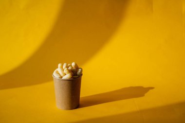 Renkli arka planda bir bardakta sarı mısır çubukları, bir kutu dolusu tatlı mısır çubukları, çocuklar için bir ikram, sarı arka plan, minimalizm