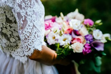 Gelin buketi, düğün buketini elinde tut, saten kurdeleler gül buketini süsle, gelinin elbisesinin arka planında, bir çiçekçi tarafından yapılan taze çiçekler, çiçeklerin kokusu...