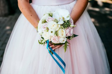 Gelin buketi, düğün buketini elinde tut, saten kurdeleler gül buketini süsle, gelinin elbisesinin arka planında, bir çiçekçi tarafından yapılan taze çiçekler, çiçeklerin kokusu...