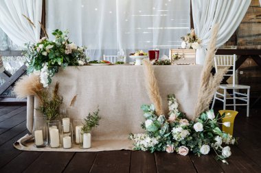 Düğün masasının dekorasyonunda çiçekler ve mumlar, düğün dekorasyonu, doğal malzemelerden yapılmış masa örtüsü, masa takımı..