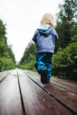 Mavi ceketli bir çocuk patika boyunca yürüyor. Küçük bir çocuk tek başına dağa tırmanır. Çocukların doğa yürüyüşü.