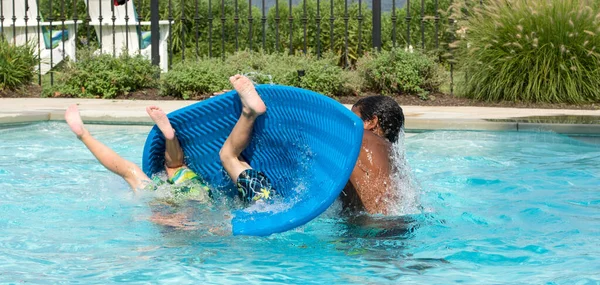 3 boys of mixed ethnicity horse-playing in a swimming pool with legs and feet up as they are dunked.