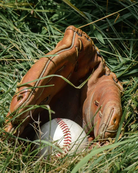 Baseball glove and ball in the grass.