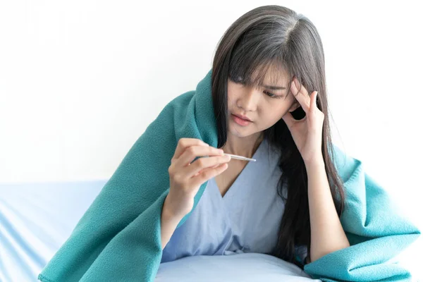 Asian woman cover with green blanket measuring temperature her body on hospital bed. Girl worry with symptom of Coronavirus Disease 2019 check fever. SARS