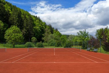 Bahar tadilatından sonra tenis kortunu kırmızı kumla temizledi.