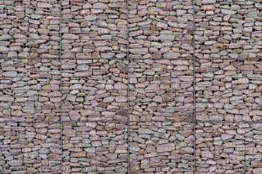 Gri doğal taşlarla dolu, hafif kavisli bir şekle sahip büyük çok katlı gabion