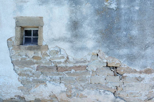 Old rundown house wall with a small window with stone surround