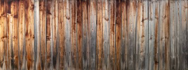 Dikey tahtalardan yapılmış eski, yıpranmış, gri kahverengi ahşap bir duvarın panoramik ayrıntıları