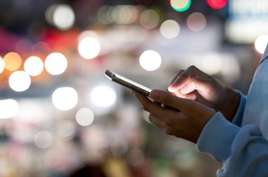 Ekran telefonundaki işaret parmağı, kısa mesaj gönderen kişi, hippi akıllı telefon ışıklı gece şehrinde mavi ekrana dokunuyor, cep telefonundaki kızları kullanıyor, interneti kapatıyor, internete bağlanıyor.