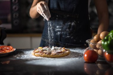Önlükteki insan elinin yakın çekimi hamuru siyah ahşap bir masaya yoğur, un serp. Fırında elle para kazan..