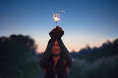 Kutlama arkaplanı için soyut bulanık kıvılcımlar, elinde yanan Noel parıltısı ve alacakaranlık arkaplanı olan rüzgar tarafından bulanık bir kadın hareketi..