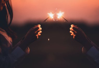 Kutlama arkaplanı için soyut bulanık kıvılcımlar, elinde yanan Noel parıltısı ve alacakaranlık arkaplanı olan rüzgar tarafından bulanık bir kadın hareketi..