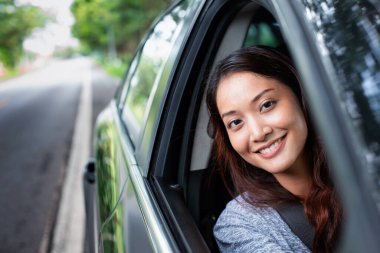 Güzel Asyalı kadın gülümsüyor ve eğleniyor. Yolda araba sürüyor.