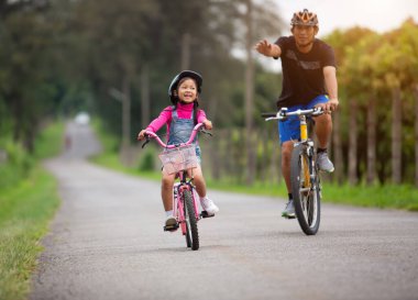 Mutlu aile babası, kızına parkta bisiklet sürmeyi öğretiyor. .