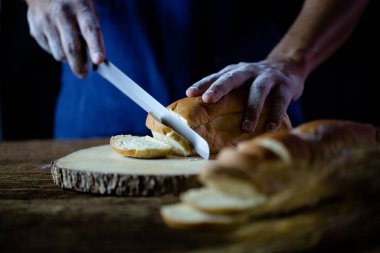 Erkek eller tahtanın üzerinde buğday ekmeği kesiyor. Geleneksel ekmek dilimlere bölünür