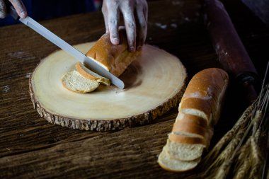 Erkek eller tahtanın üzerinde buğday ekmeği kesiyor. Geleneksel ekmek dilimlere bölünür