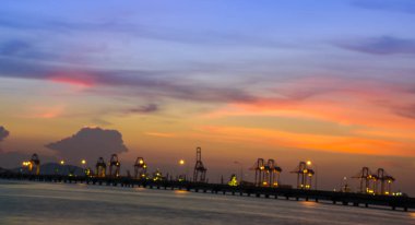 Gün batımı ya da gün doğumu, güzel sarı-turuncu gökyüzü okyanusta ya da kargo rıhtımlı denizde. Şehir manzarası konsept resmi